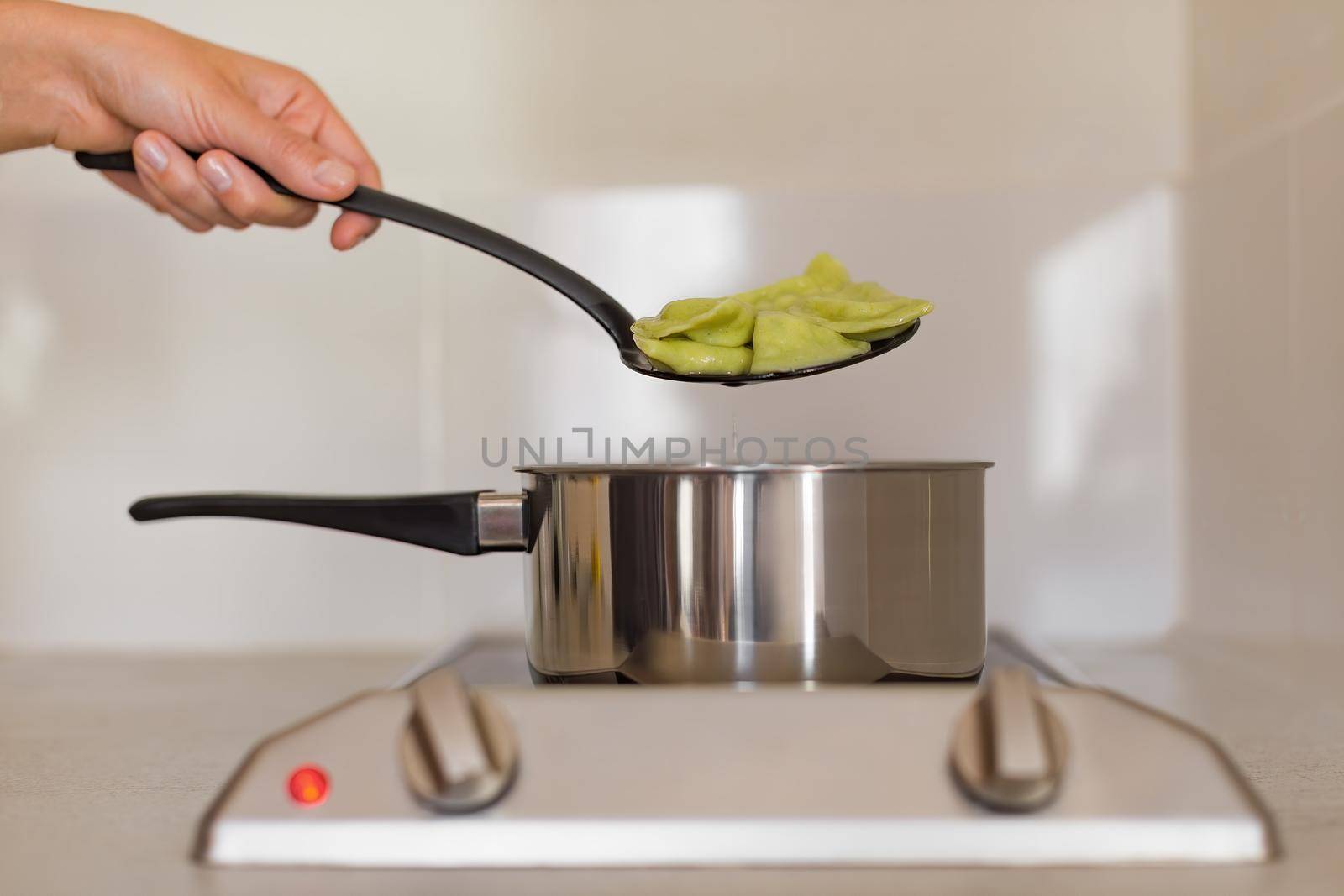 A hand with a hollowed spoon takes out green vegetarian dumplings from the ladle, which is standing on the stove