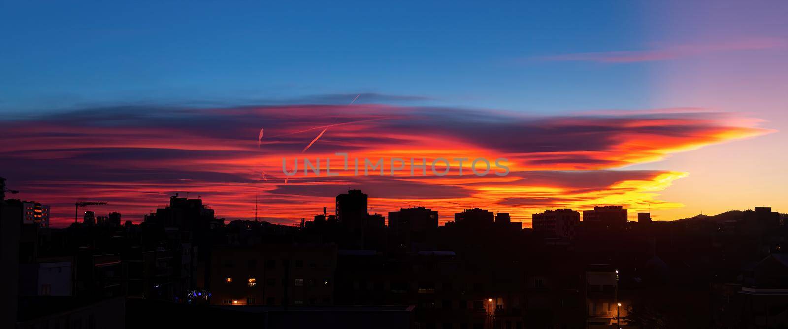Amazing sunset with orange, pink and red stratus clouds over the city with traces from the plane in the sky. Background for forecast and meteorology concept. Barcelona, Spain.