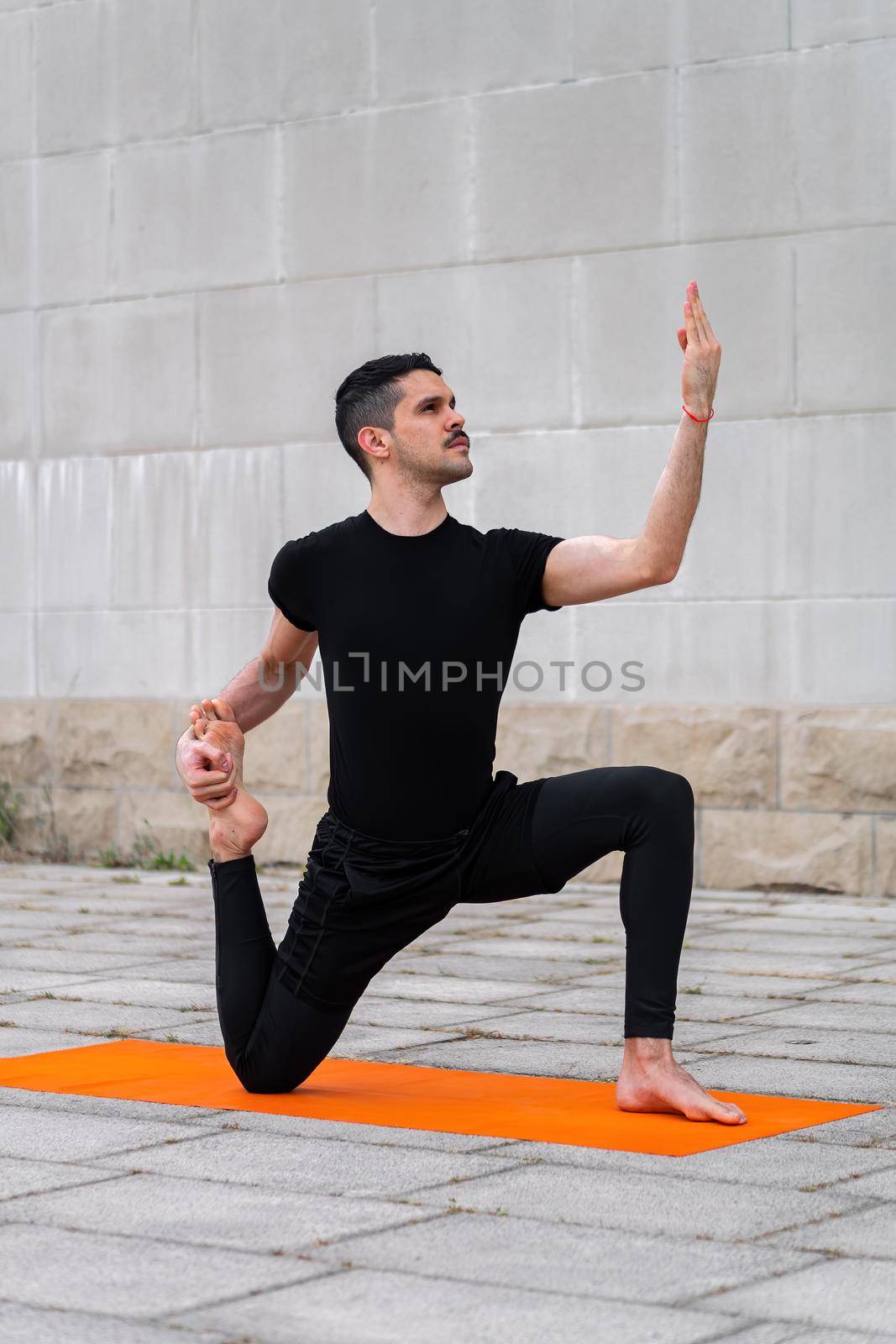 Handsome sporty latin man exercising in a city, doing yoga, fitness or pilates training, preparing for One Legged King Pigeon Pose - Eka Pada Rajakapotasana