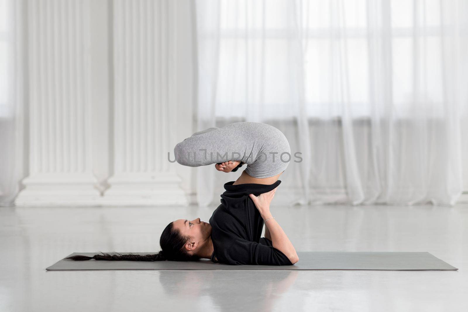 Young attractive asian woman practicing yoga concept, Urdhva Padmasana Upward Lotus in shoulderstand exercise, working out wearing black sportswear pants, white studio background.