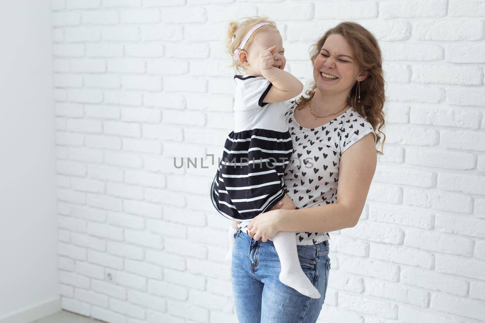 Mother helps her deaf baby daughter putting hearing aid in little girl's ear indoors - cochlear implant and innovative medical technologies