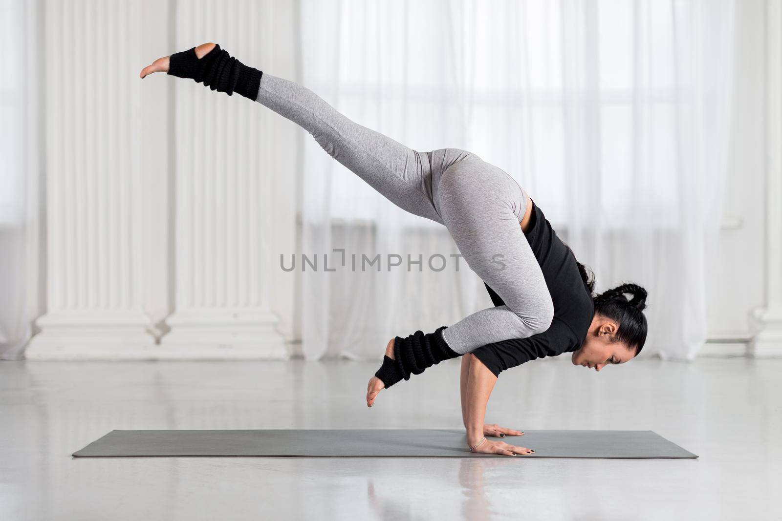 Asian woman working out in white hall, doing arm balancing handstand yoga asana, One Legged Crane Pose, Half Crow Pose, eka pada bakasana.