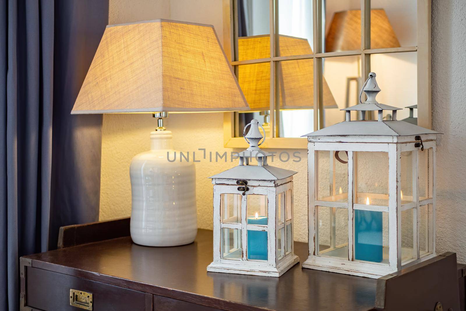 Vintage wooden lanterns, candle holders with blue burning candles inside, placed on dark table with lamp in a cozy room.