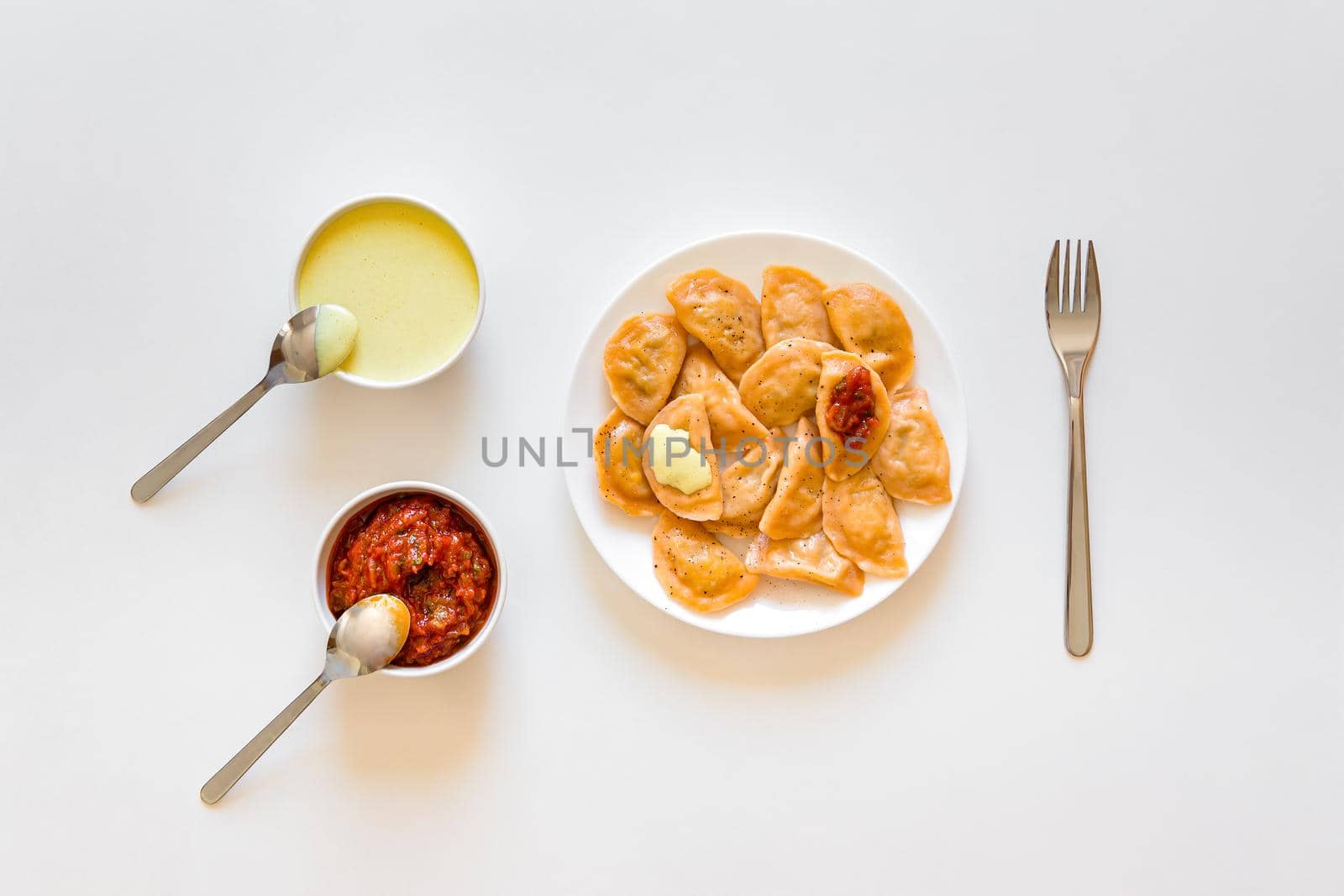 Traditional russian and ukrainian food vareniki dumplings with mustard and tomato sauce. Dough made red with tomato paste. Placed on white table. Top view.