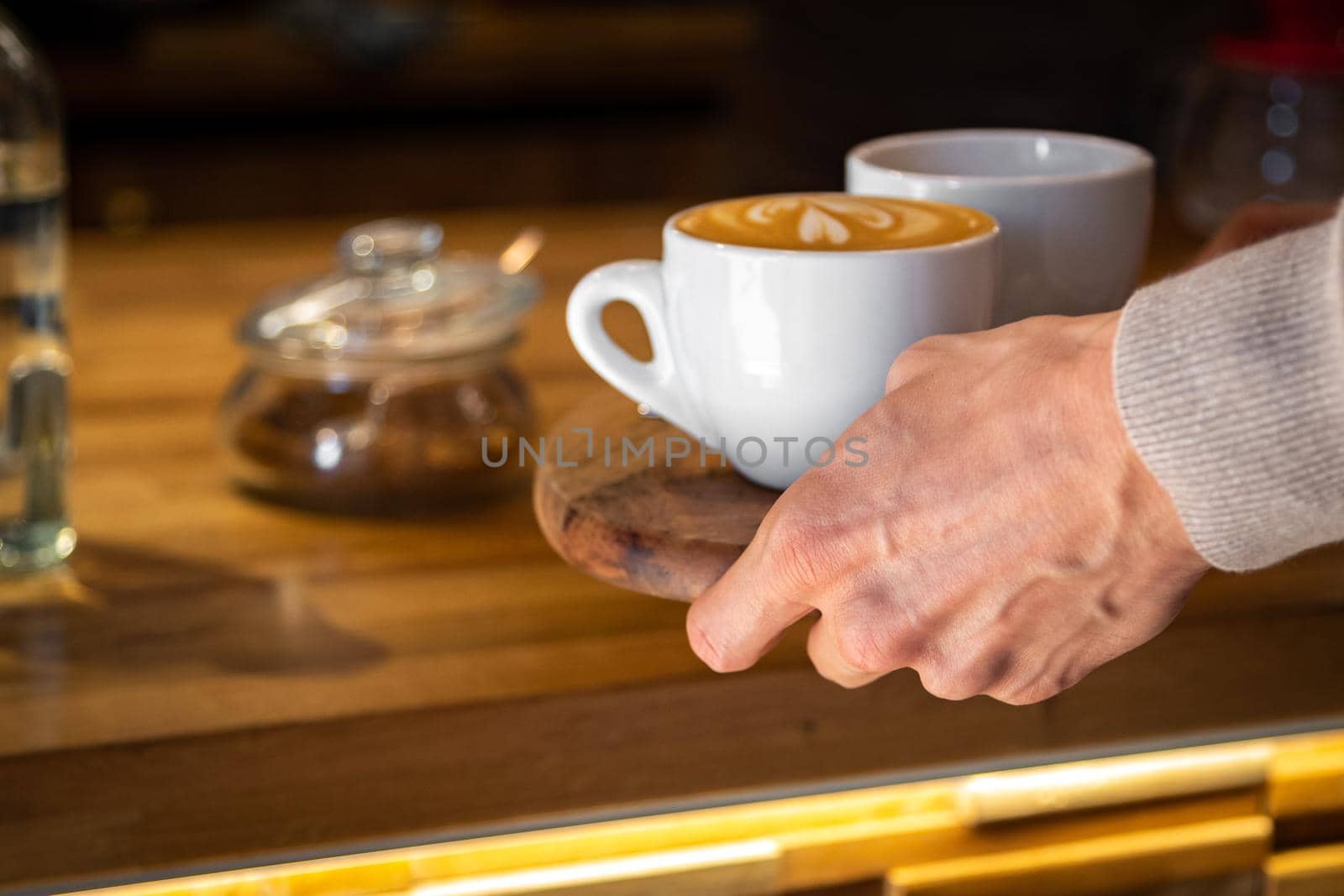 Close up of male hand taking cup for hot coffee with heart latte art on wooden tray in cafe shop