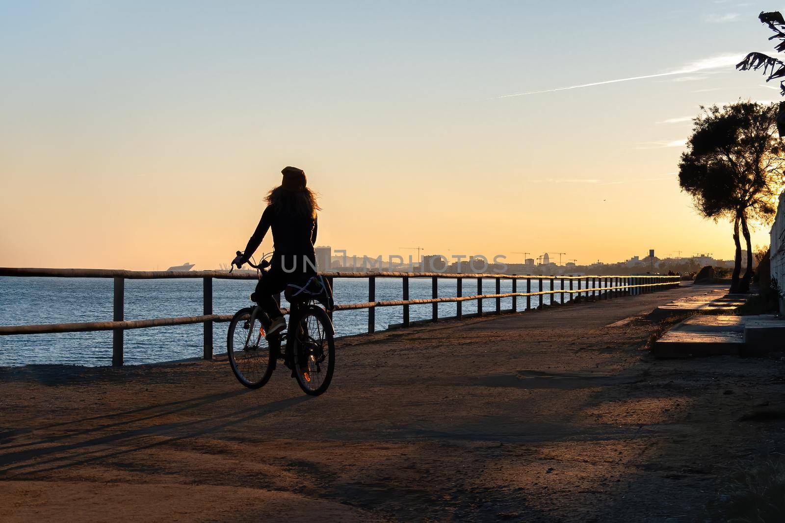 Silhouette of young curly girl riding a bicycle at the sunset on the promenade road of Maresme, Catalonia, Spain by apavlin