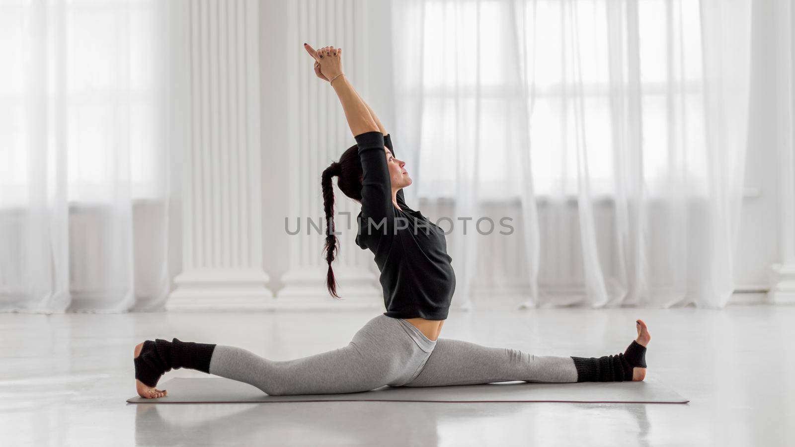 Attractive young asian woman practicing front splits or Monkey Pose on gray mat at yoga studio. Hanumanasana.