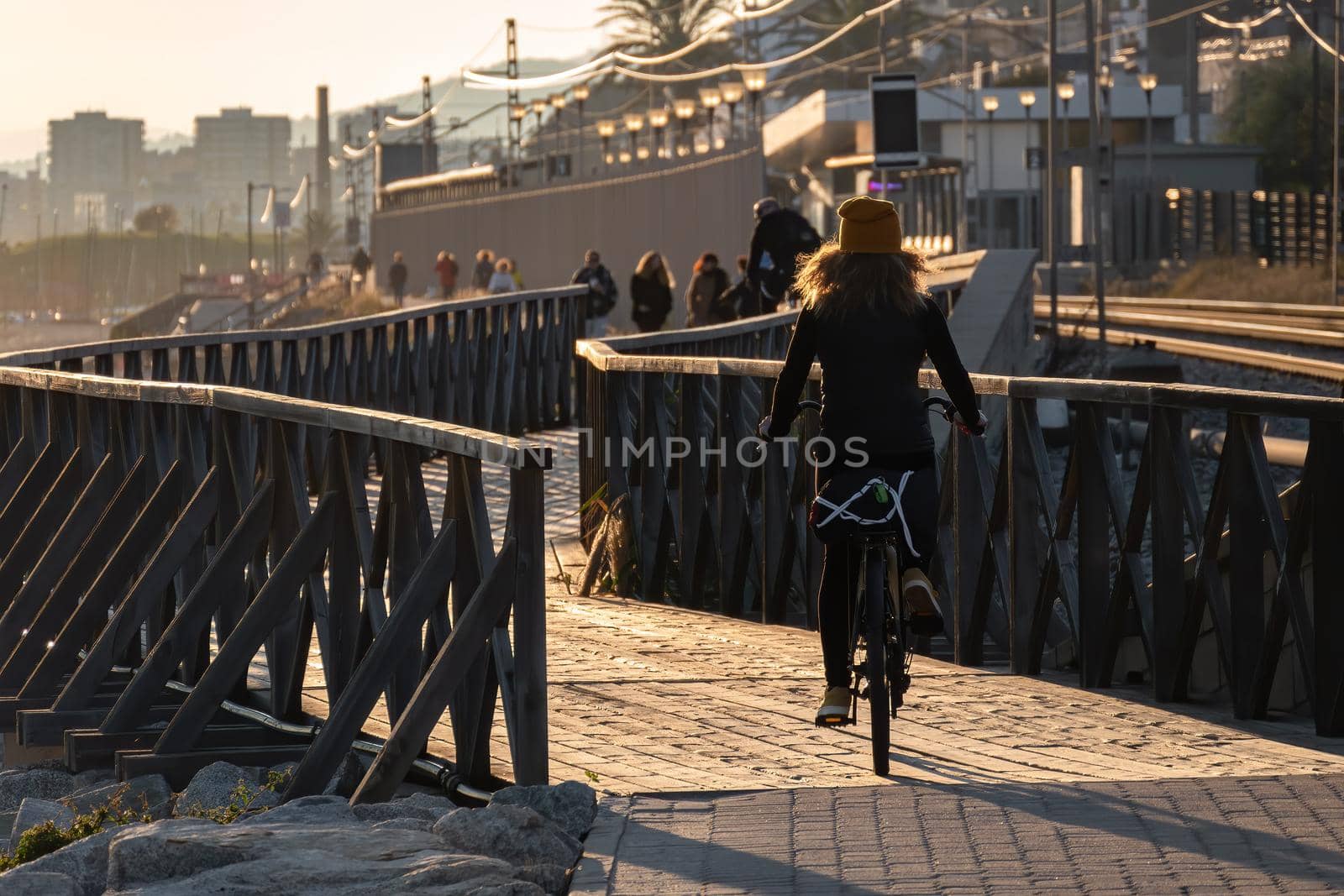 Young girl with curly hair fluttering in the wind is riding a bicycle on wooden bridge at sunset on the promenade road by apavlin