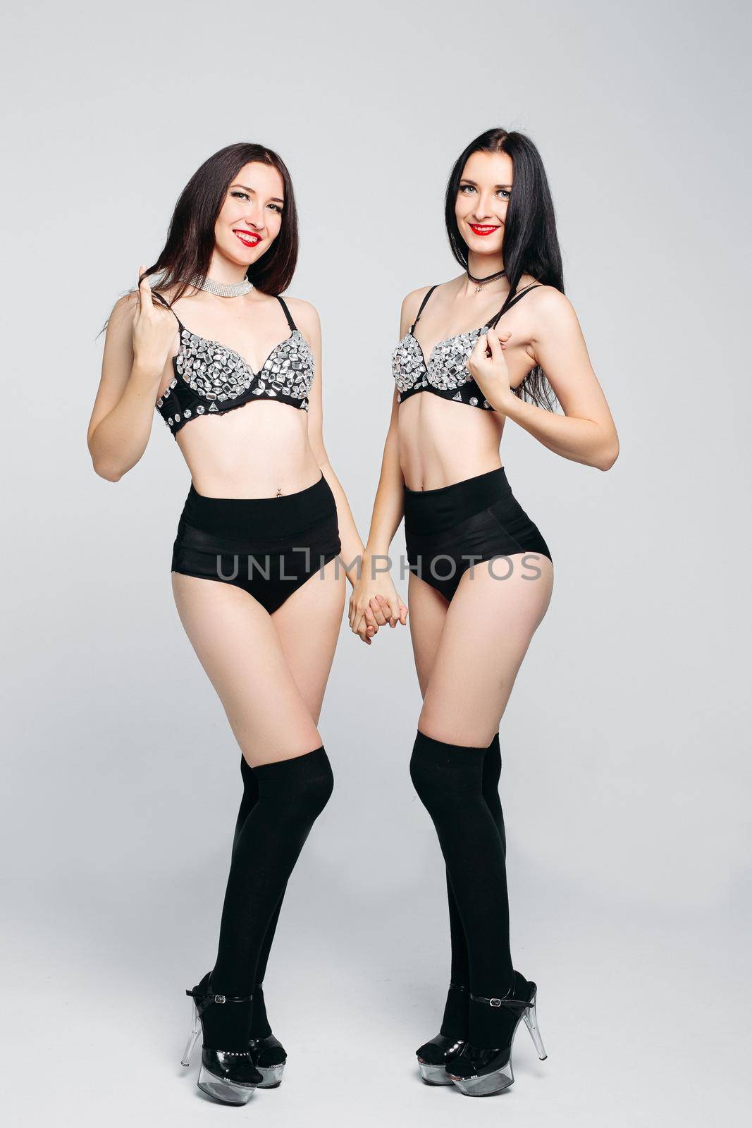 Seductive sisters twins in shine and glamorous lingerie posing with crossed hands at camera. Beautiful dancing ladies after beauty salon, before party. Night club and lingerie concept.