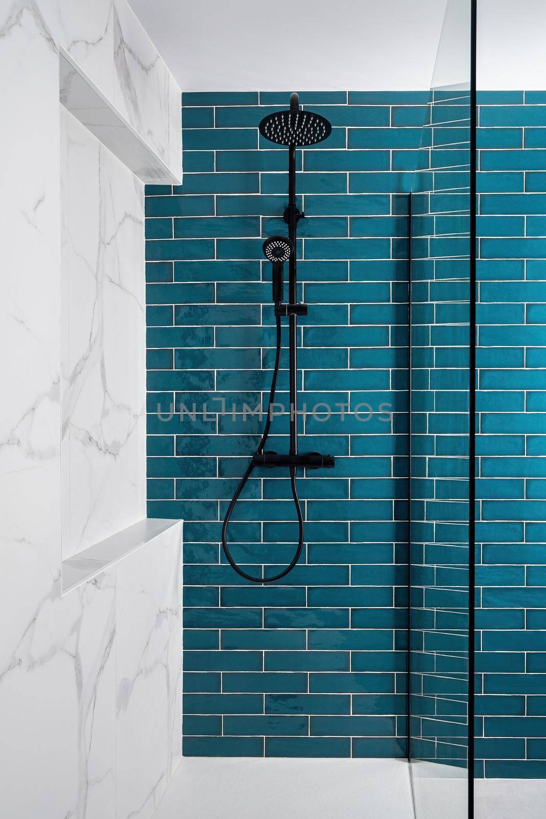 Modern tiled shower with rain head, hand held shower and glass door. Dark aquamarine and white and color in the bathroom.