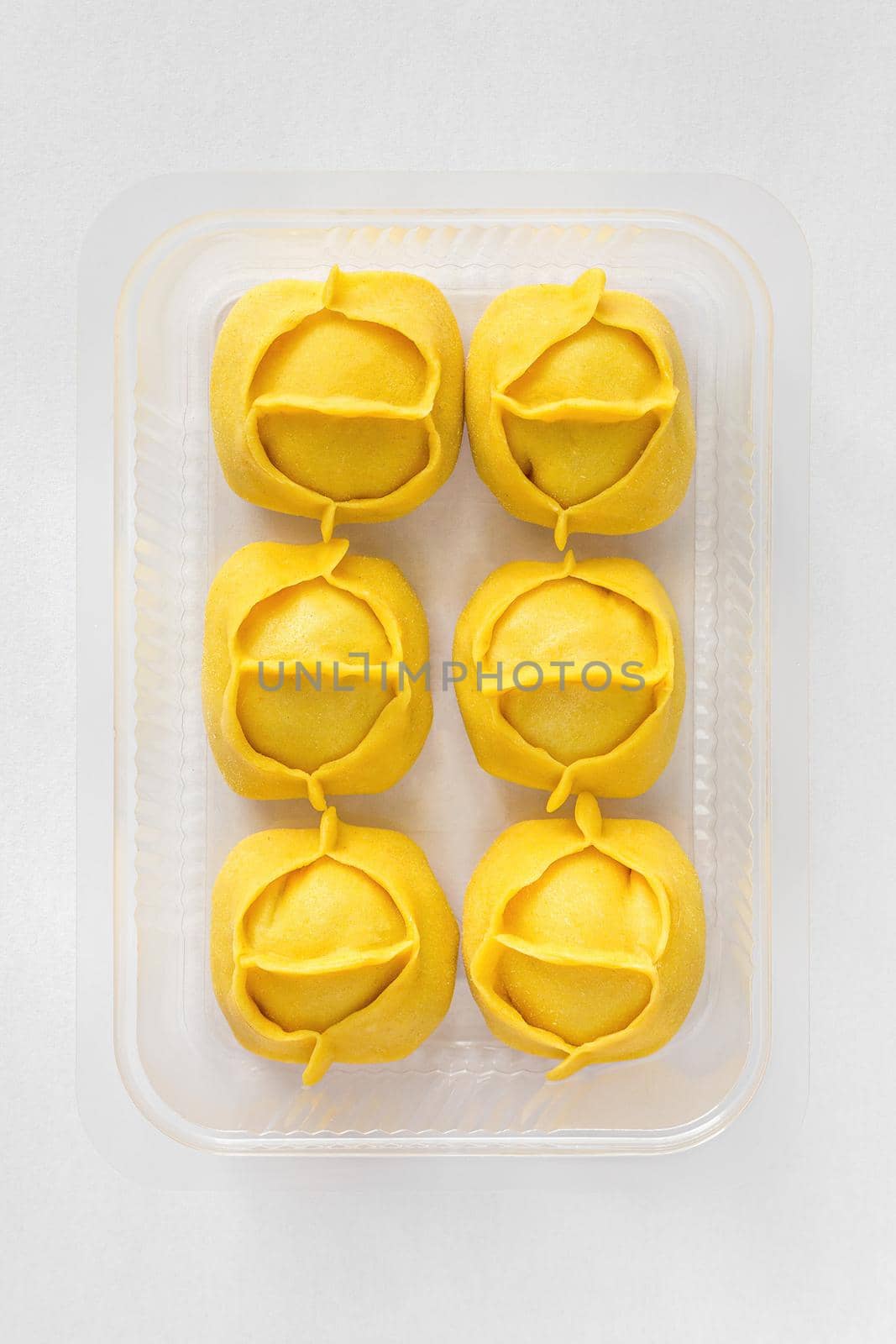 Big yellow dumplings portion in plastic container for sale. For steam cooking. Manti, Manty. Dough colored yellow with curcuma