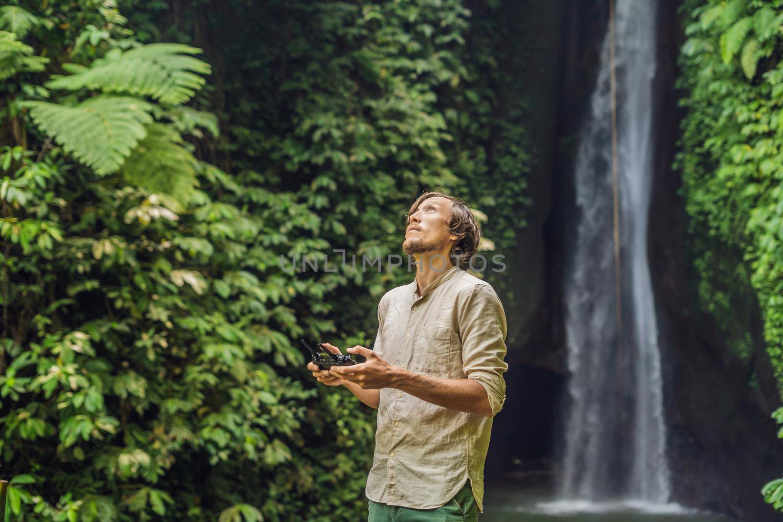 The man controls the drone against the background of the forest and the waterfall.