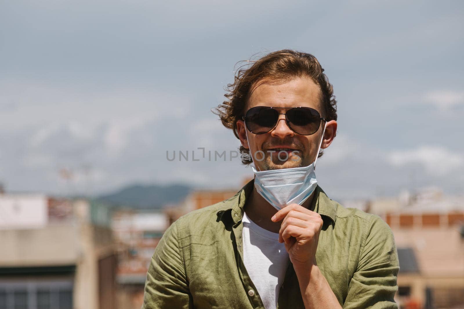Young beautiful european man takes off protective medical mask from face. Happy and smiling positive guy in sunglasses at the end of pandemic quarantine.