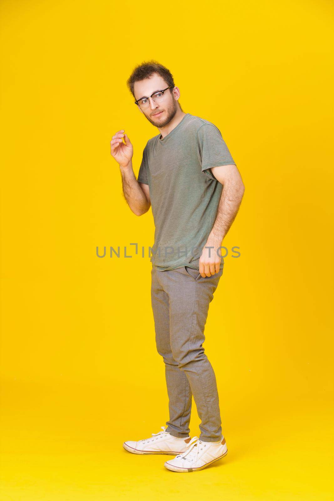 Handsome young man in casual wear in glasses posing on yellow background with one hand up. Stylish bearded smart casual look hipster man. Thoughtful young man on yellow background by LipikStockMedia