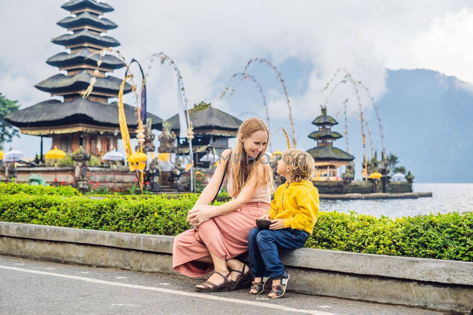 Mom and son in the background of Pura Ulun Danu Bratan, Bali. Hindu temple surrounded by flowers on Bratan lake, Bali. Major Shivaite water temple in Bali, Indonesia. Hindu temple. Traveling with children concept by galitskaya