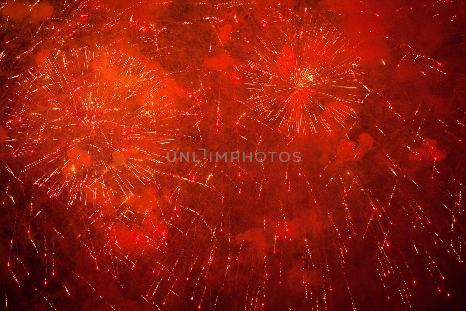 Red, orange, neon and golden sparks of fireworks in the sky and smoke from the charges
