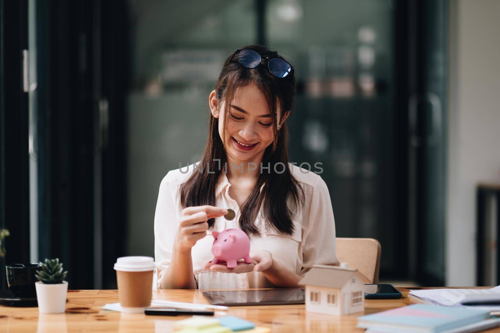 mortgage, investment, real estate and property concept - close up of woman putting money into pink piggy bank for loan or save for buy a new house.