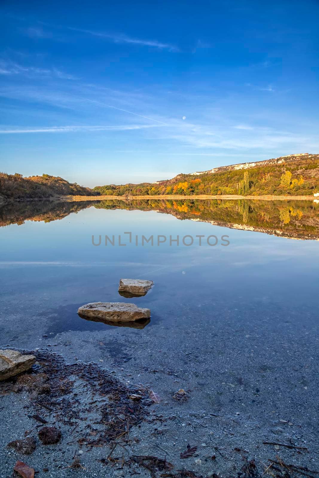 View from shore with fall foliage colors reflected in still lake water on a beautiful autumn day  by EdVal