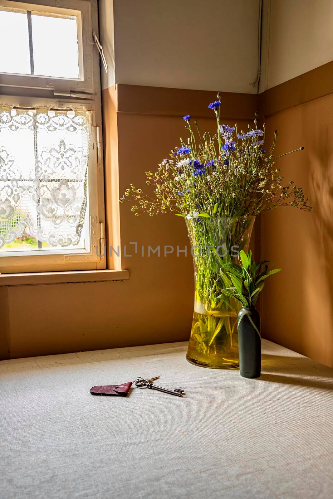 Bunch of autumn flowers in a vase on the window and keys of the home of the table in the corner of the room. Vertical view by EdVal