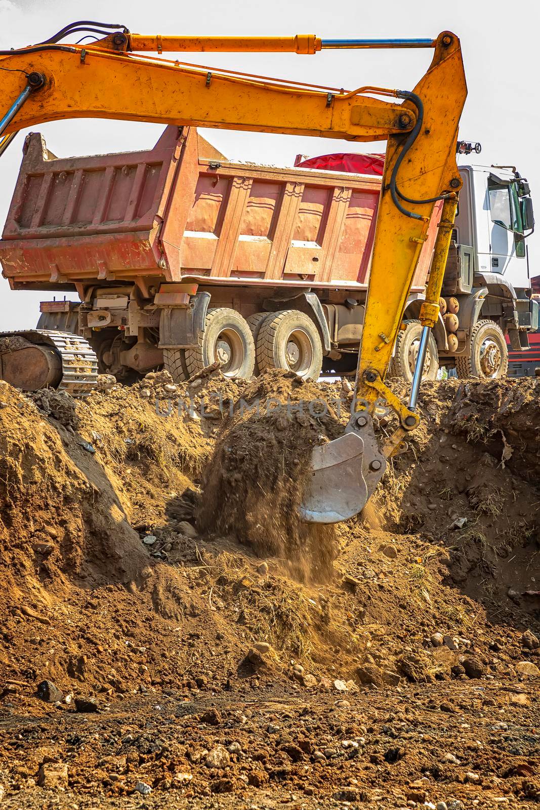 Yellow excavator and empty dump truck working at the construction site. Vertical view by EdVal