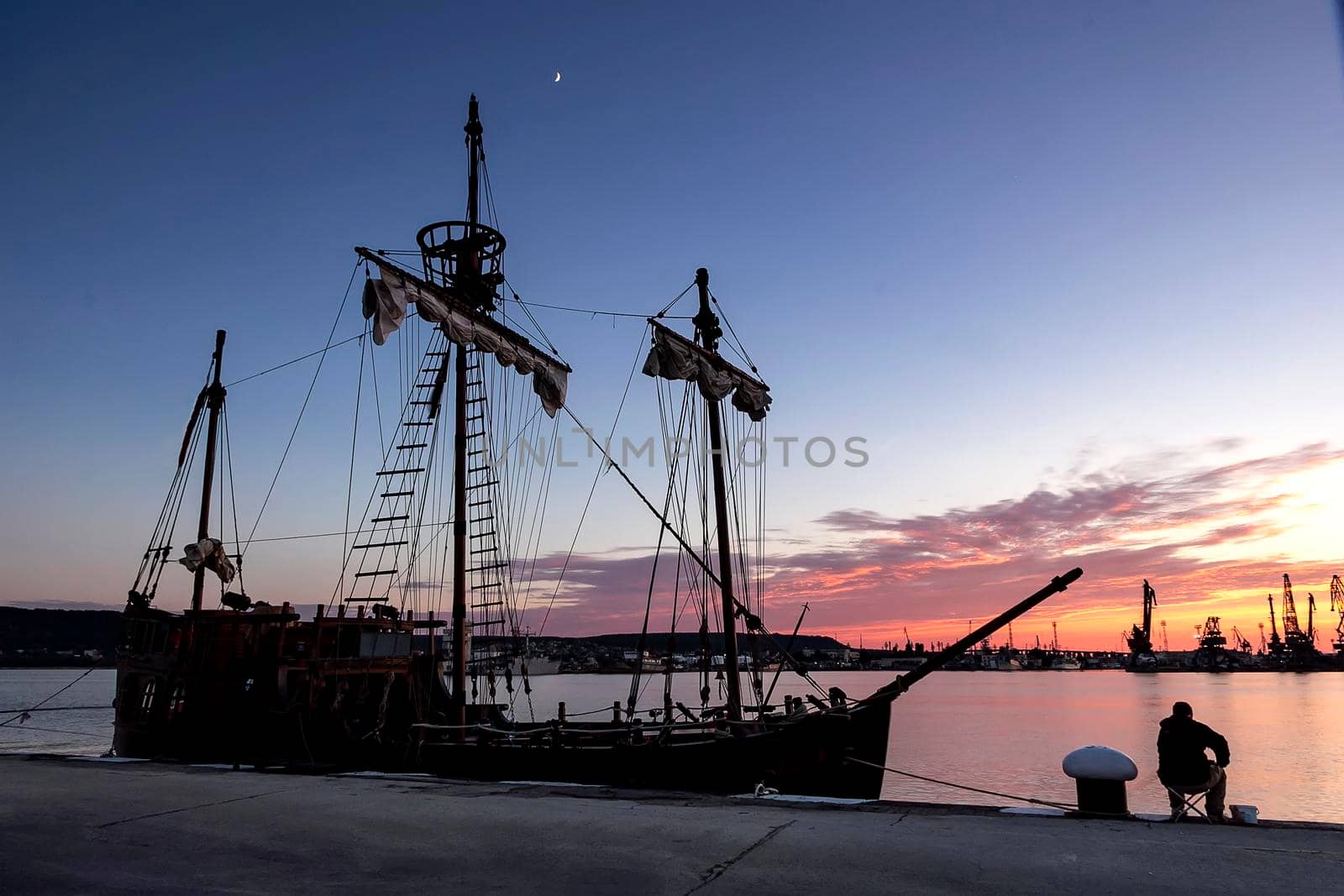 Silhouette photo of sailing ship moored in the port and fisherman in the evening