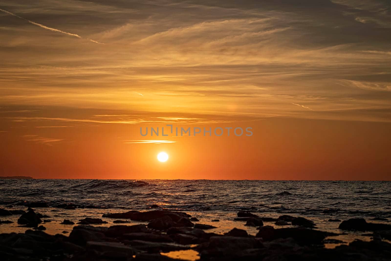 Stunning morning seascape with sun and stones on the water