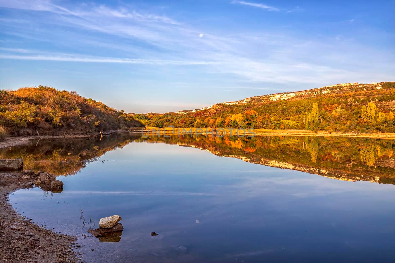 Colorful tree line on a calm lake at sunrise during autumn.