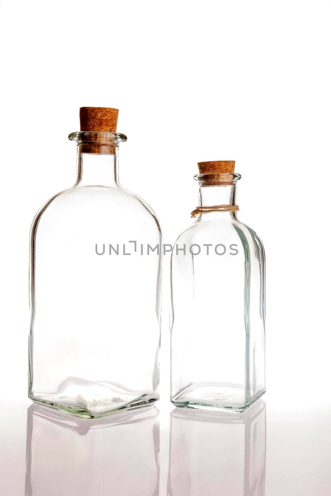 two glass bottles with cork on a white background with reflection