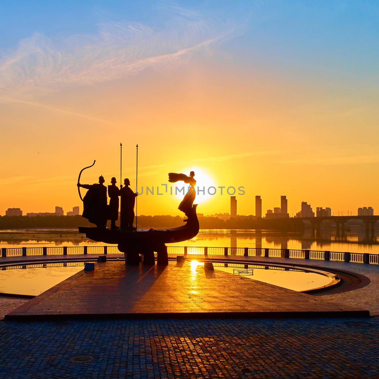 Monument to the founders of Kyiv at sunrise, wide-angle view with blue sky and yellow sun. Statue of Kyi, Shchek, Horyv and Lybid