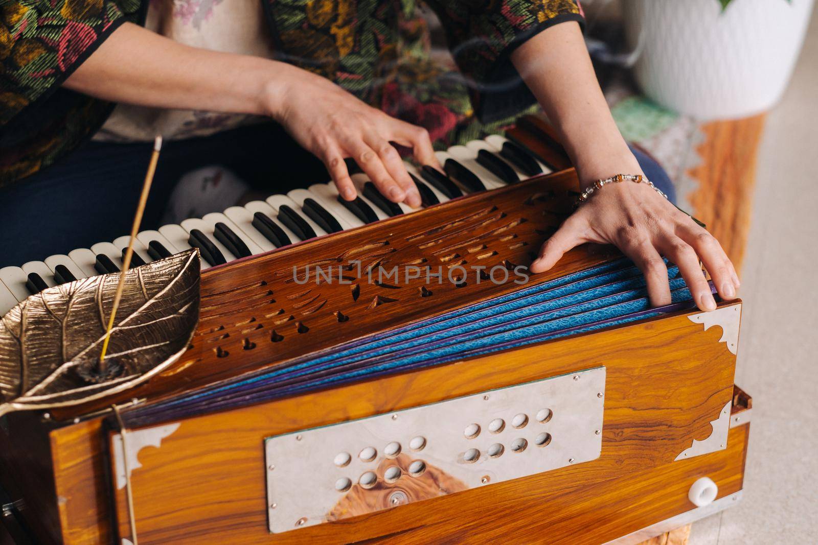 Hands of a woman sitting on the floor and playing the harmonium during the practice of kundalini yoga by Lobachad