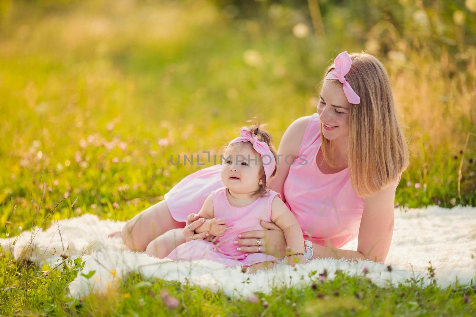 mother and daughter in identical pink dresses are sitting in nature