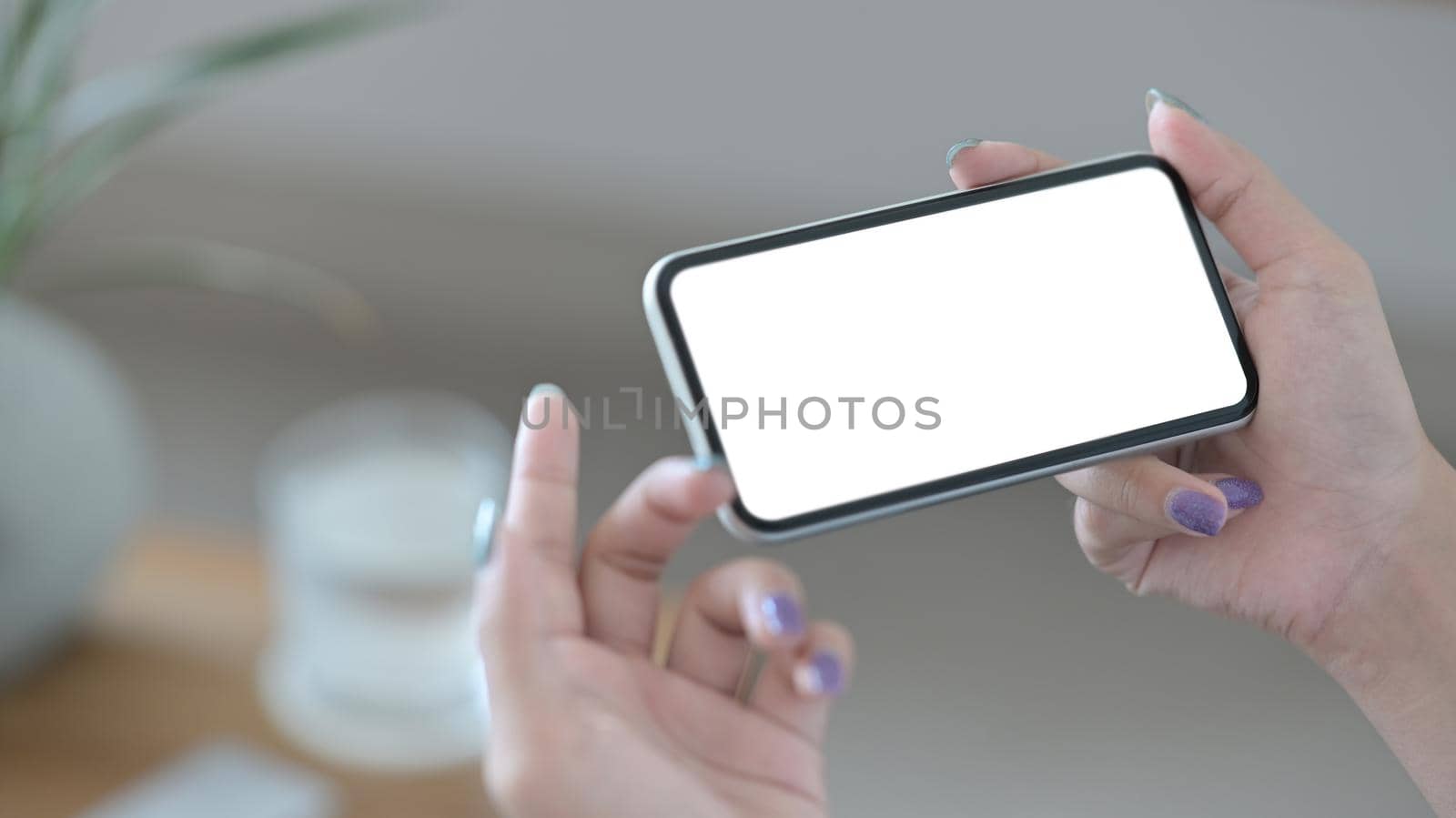 Close up view woman holding smart phone in horizontal position with empty screen for graphics display montage.