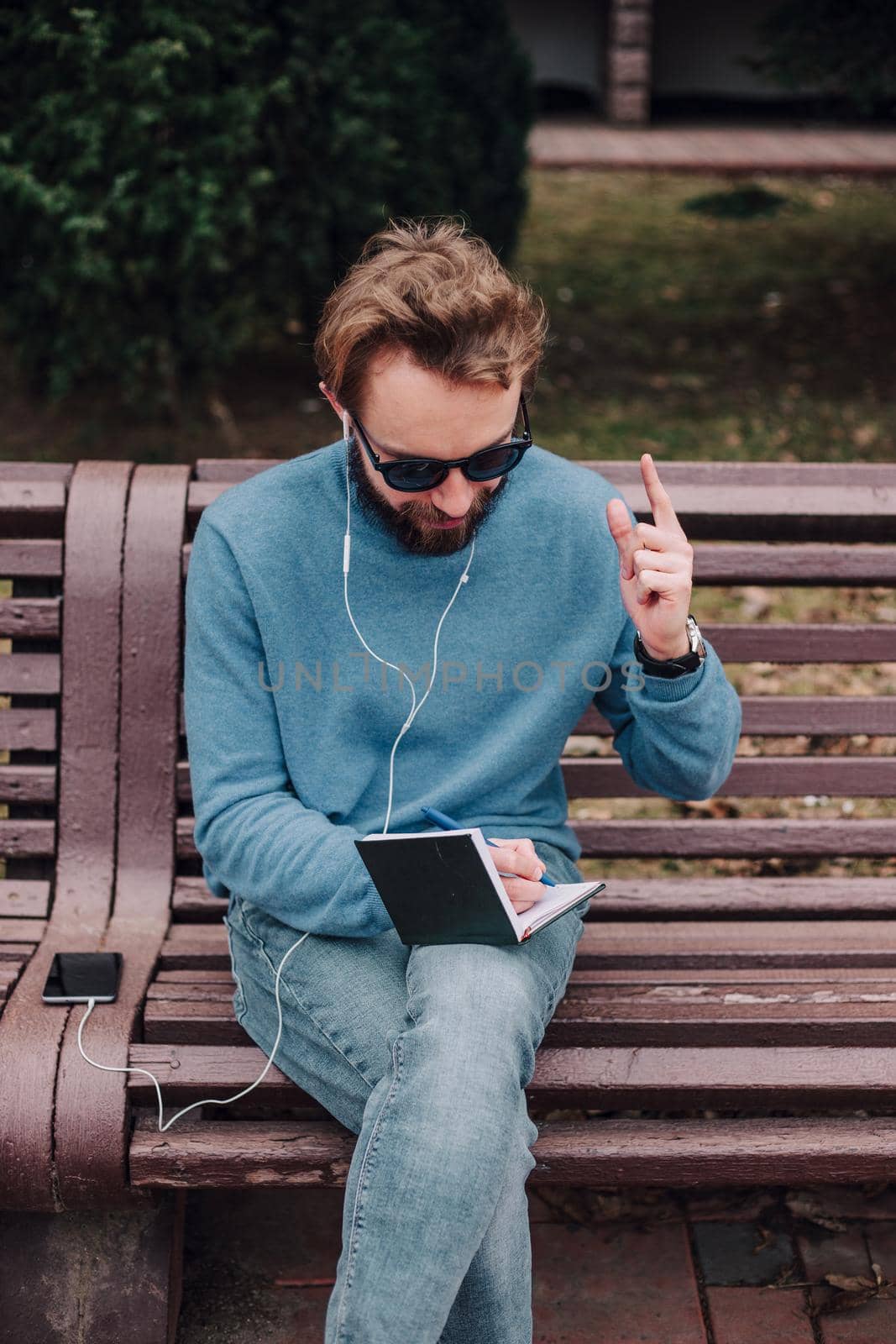 young gay hipster boy notice ideas siting in a park and listen music by headphones