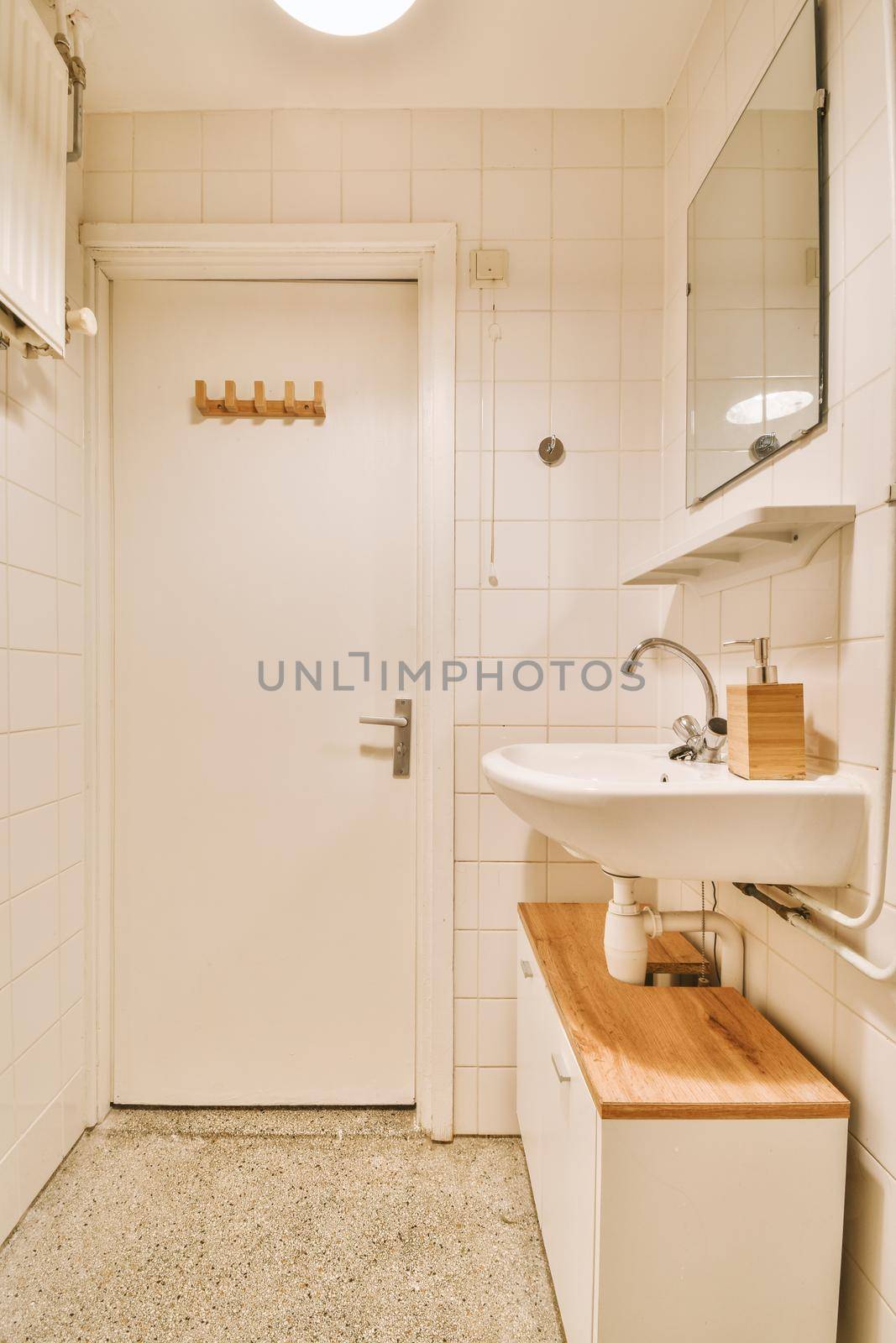 Cupboard with sink and mirror attached to tiled wall near door and drying rack in modern restroom