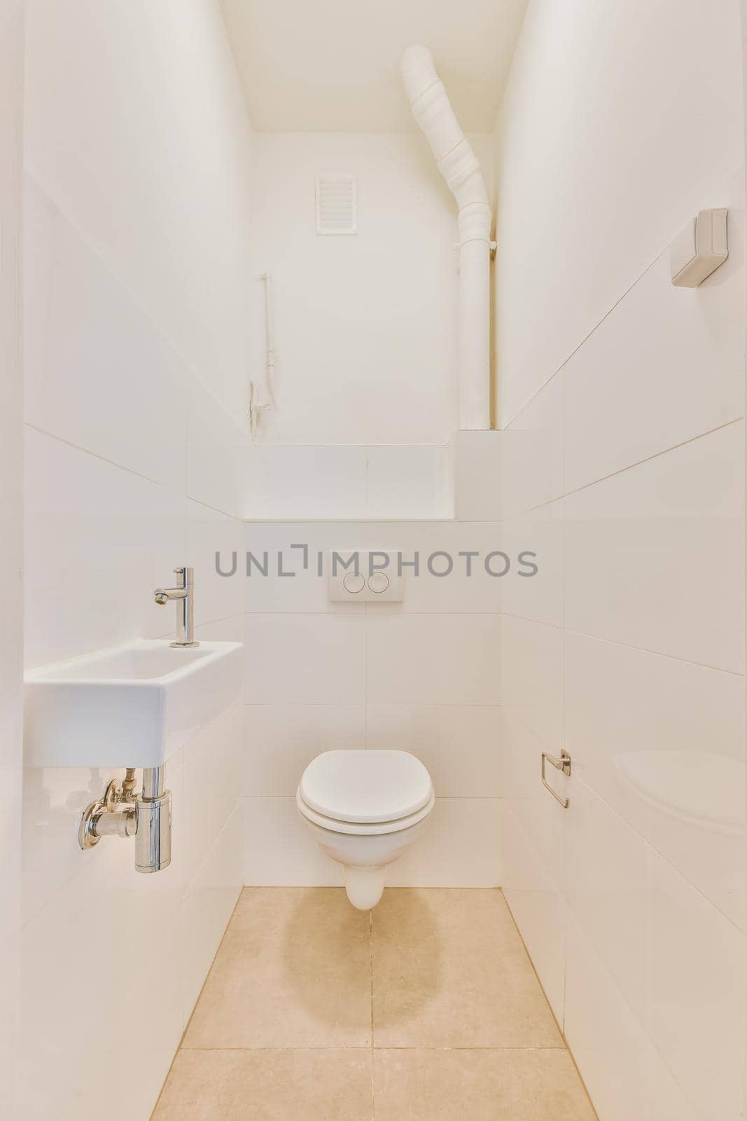 Wall hung toilet and small sink in corner in lavatory room with beige tile