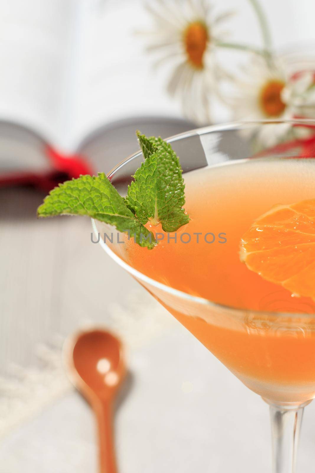 Orange jelly in the glass topped mint leaves with opened book and chamomiles on the background Close up selective focus