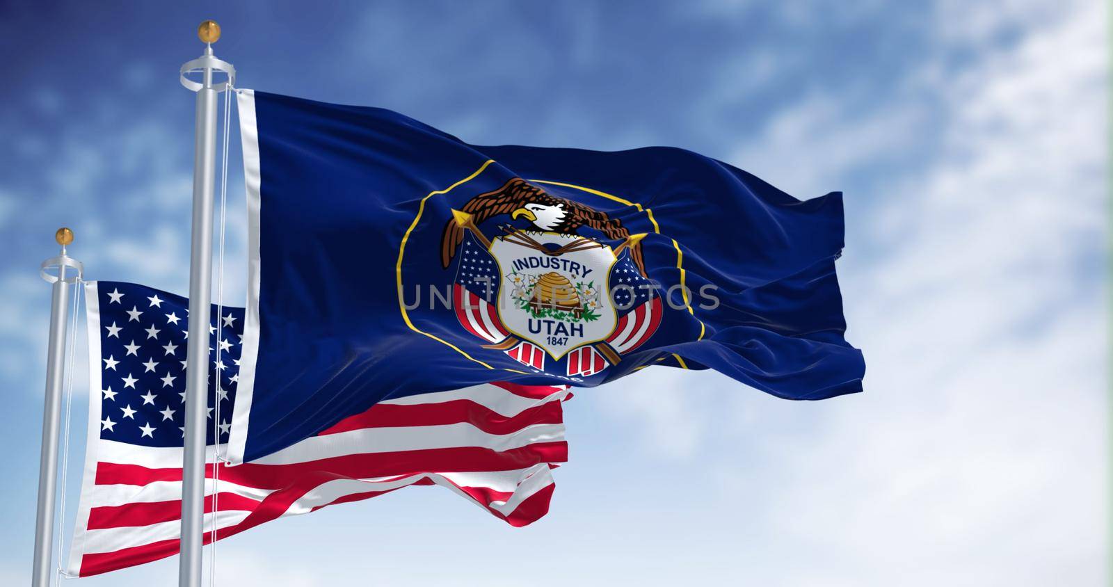 The Utah state flag waving along with the national flag of the United States of America. Utah is a state in the Mountain West subregion of the Western United States