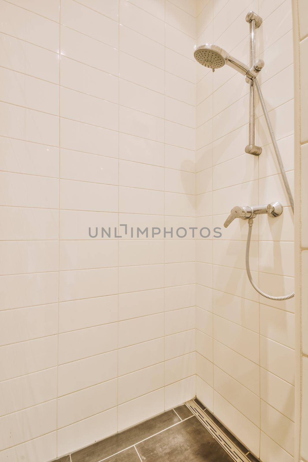 Shower faucets attached to tiled wall near glass partition and ornamental curtail in washroom at home