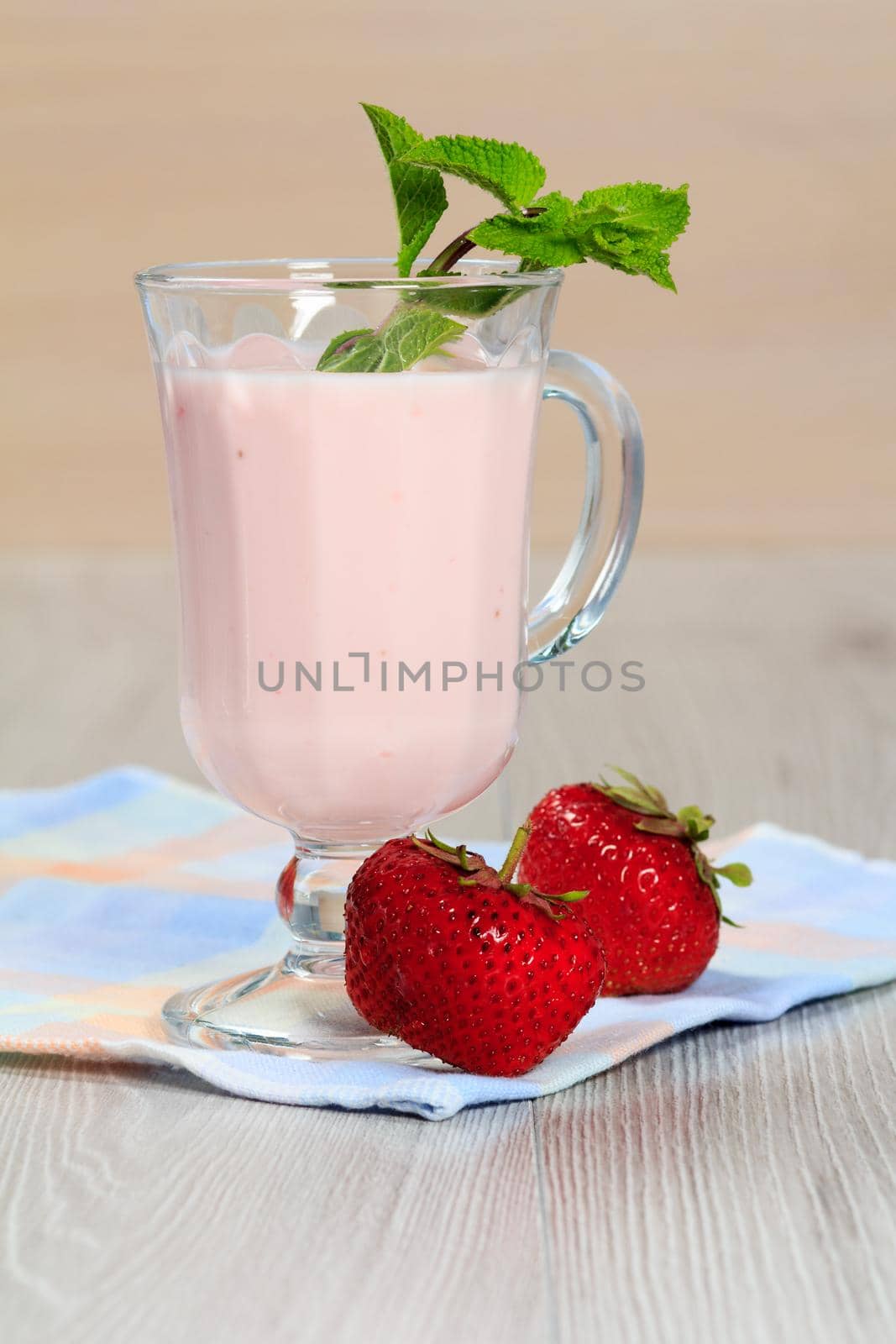 Glass of delicious yogurt with mint and fresh strawberries on white wooden table