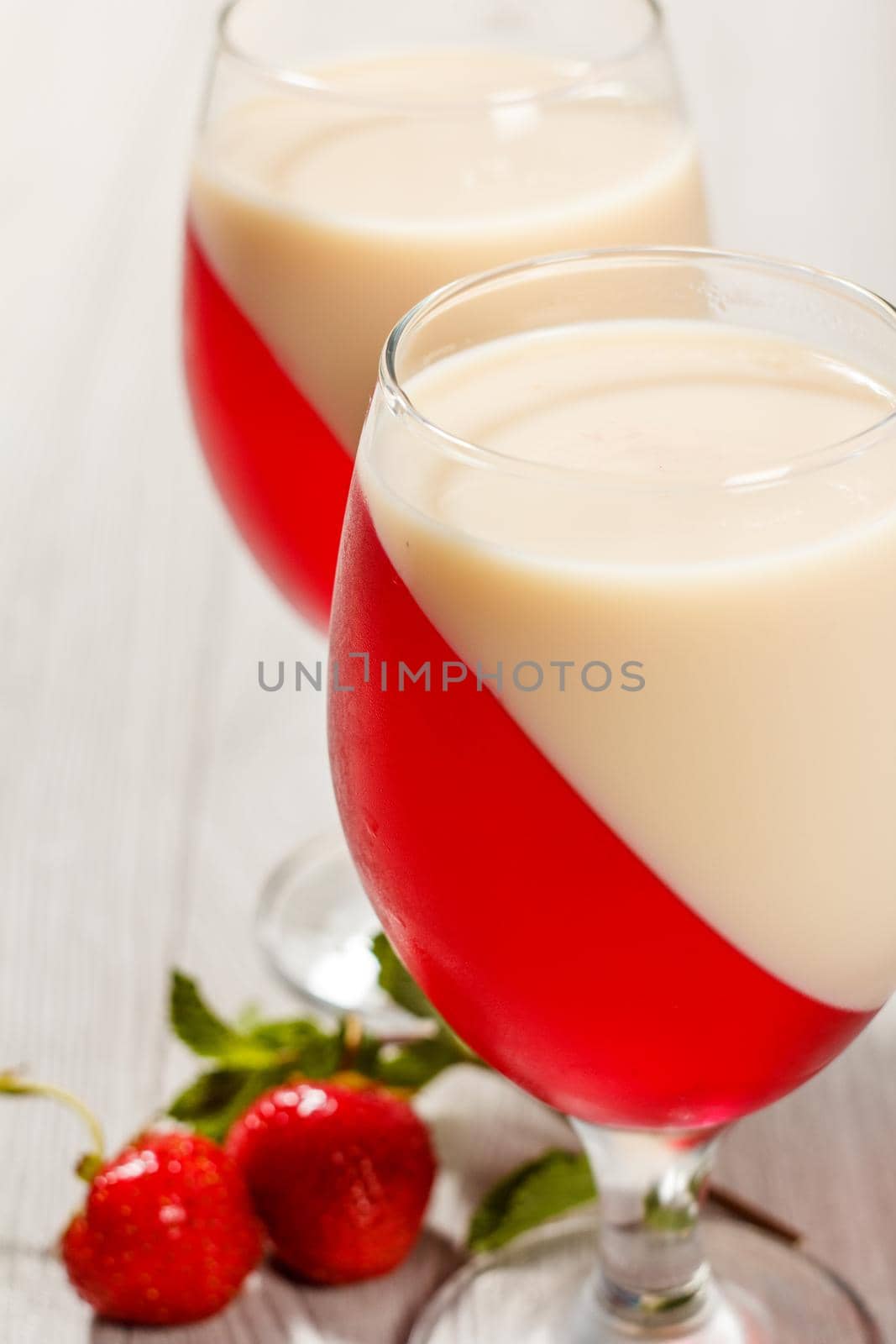 Cherry and milk jelly in the glasses with mint leaves and strawberries on the background