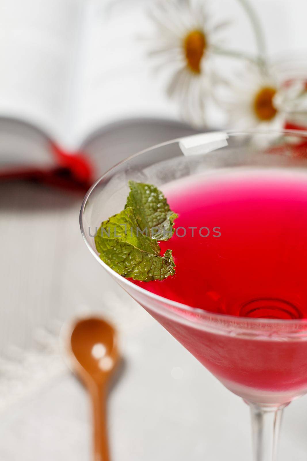 Cherry jelly in the glass topped mint leaves with opened book and chamomiles on the background Close up selective focus