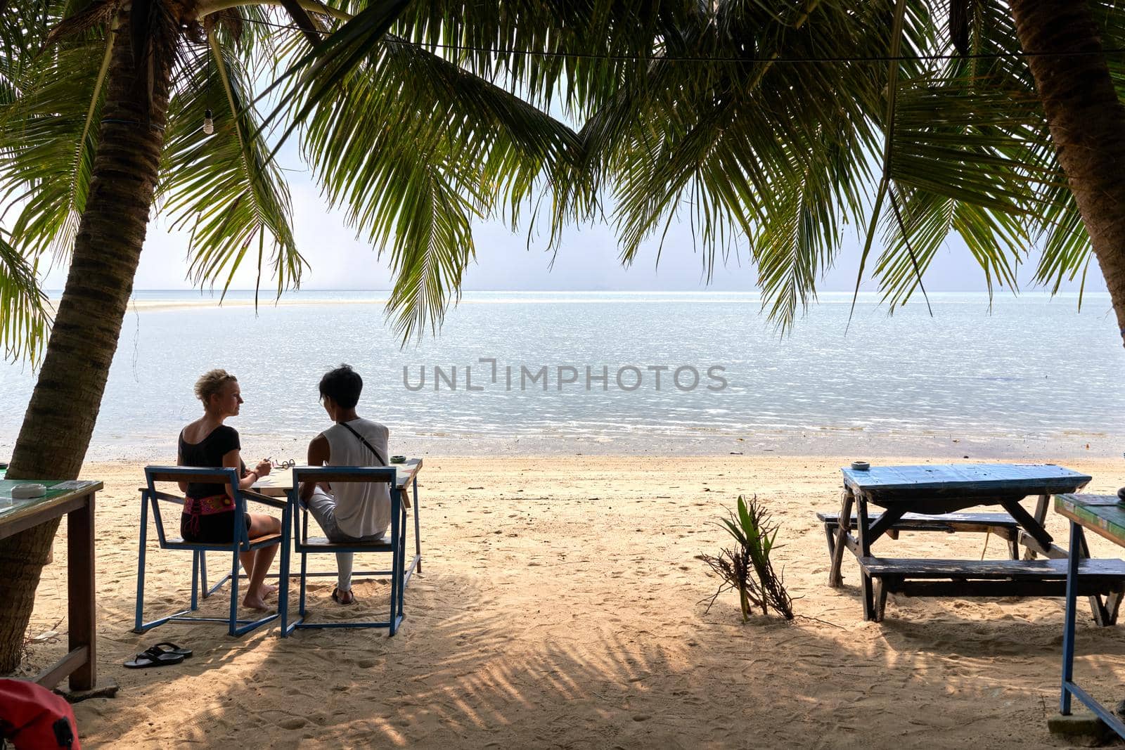 Multicultural couple sitting on a beach looking to the horizon while talking by WesternExoticStockers