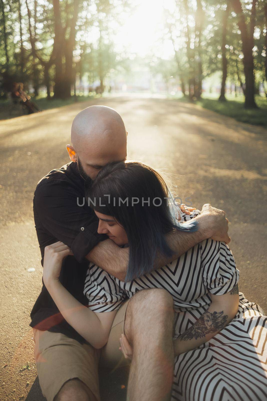 lovers sit in a hug on the asphalt against the background of the sun. the guy hugs the girl from behind by Symonenko