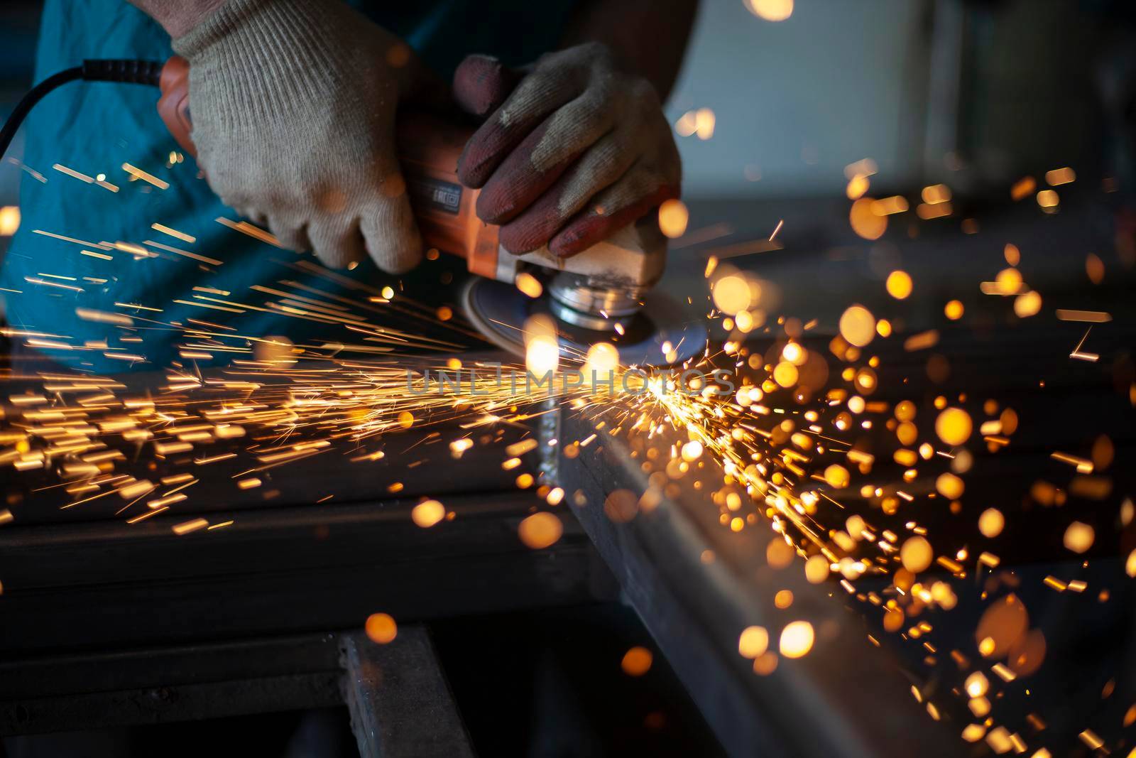 Metal cutting. Grinding steel. Work as a grinder. Sparks from friction. Men's work. Creating a design. The project in the workshop. Iron processing. Hand electric tool.