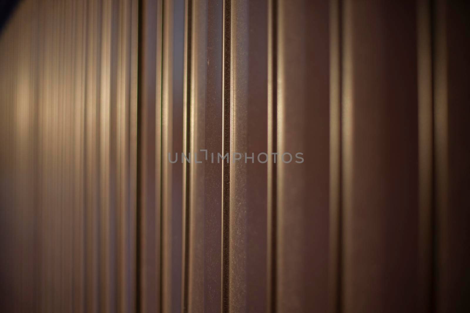 Texture of steel fence. Profile sheet is brown. Fence details. Blurry background in sunlight.