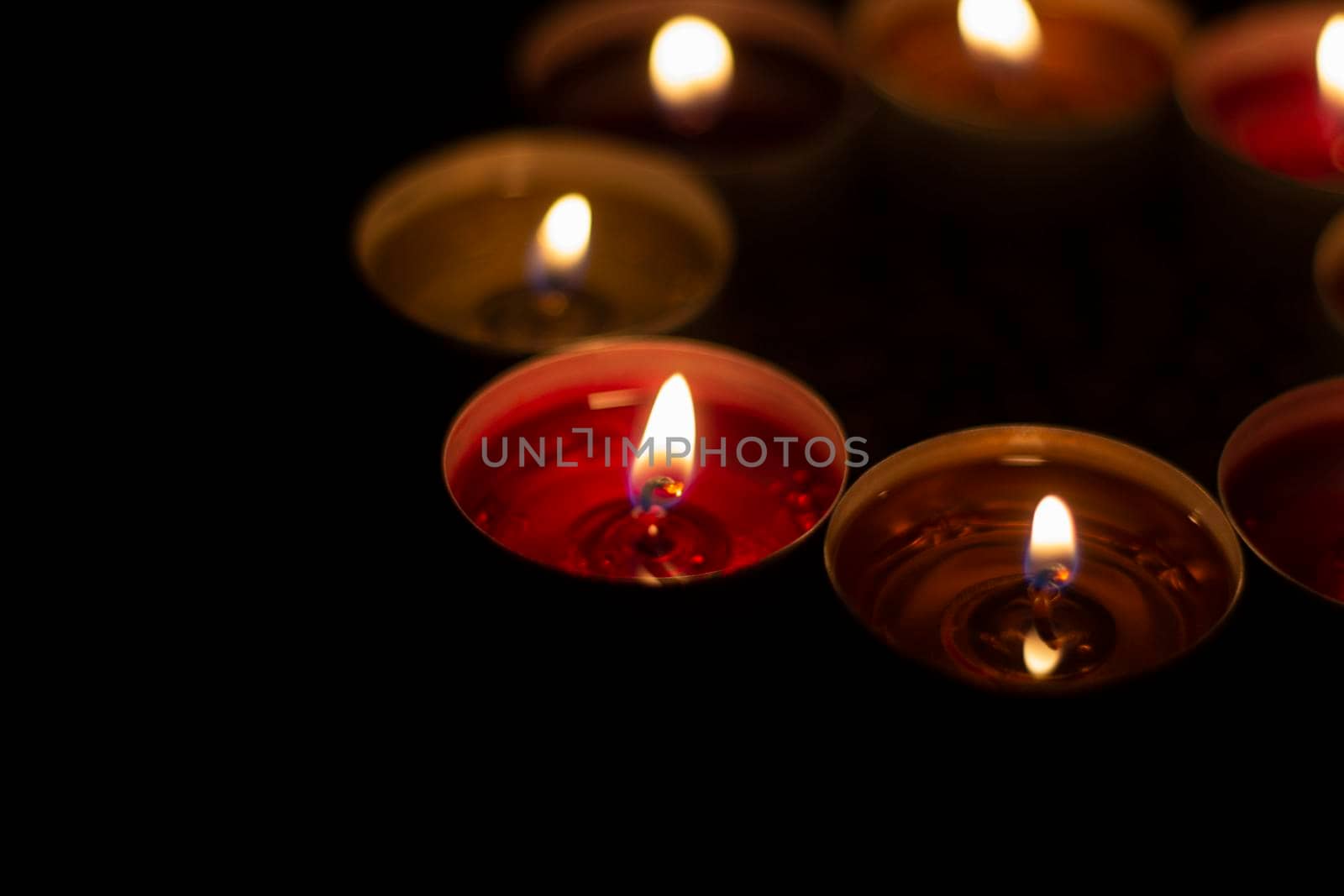 Round candles burn in dark. Wax candles on dark background. Red and yellow lights. Details of candlelit dinner.