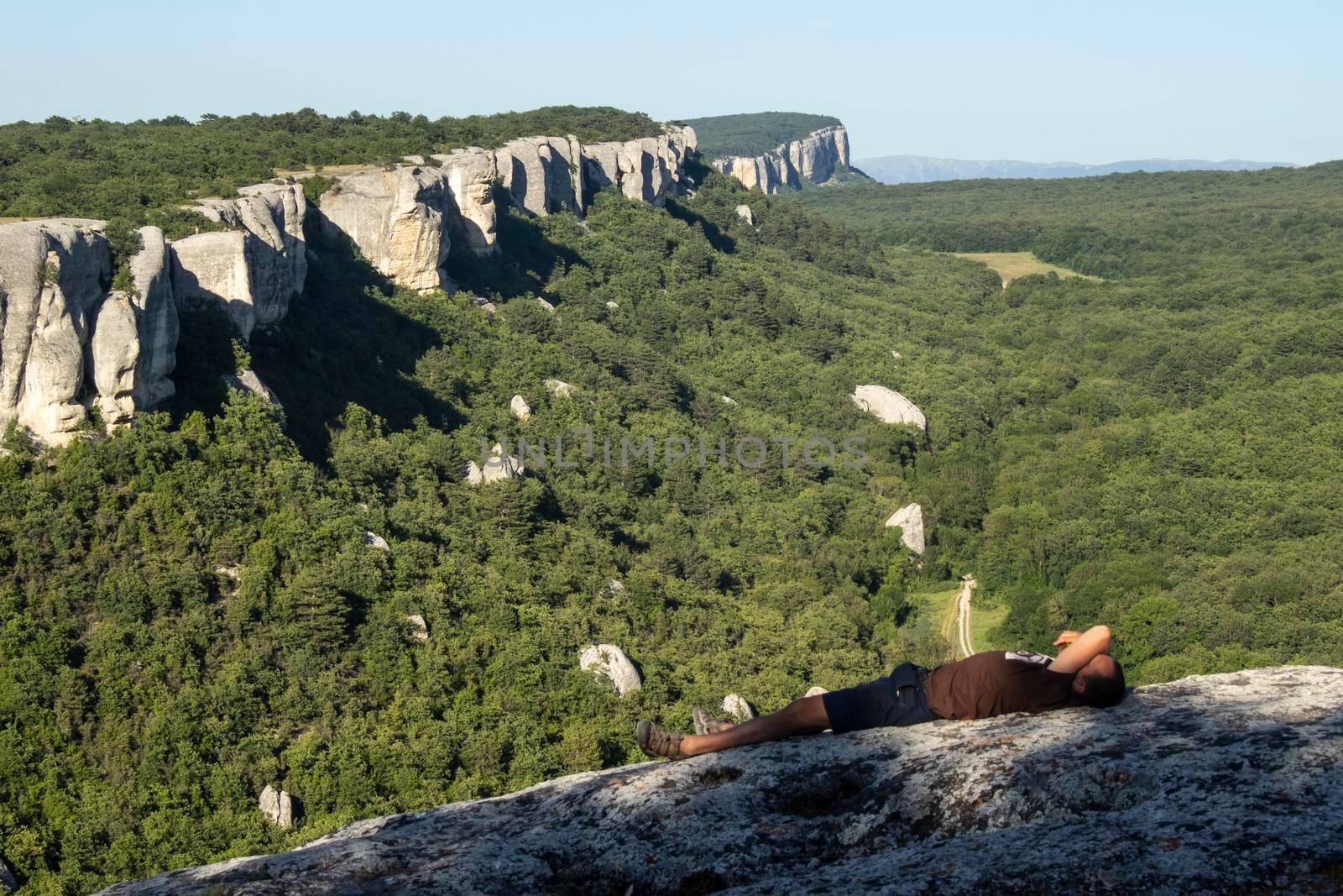 A man walks through a cave city in the summer. Tourists watch the rocks. Rest on top. Tourist route in the Crimea. Crimean mountains in the travel season. by OlegKopyov