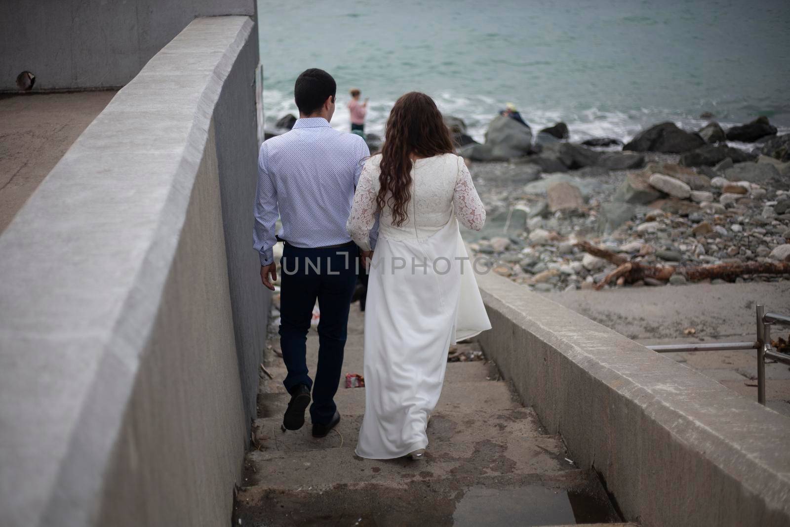 Guy and girl go to sea. Bride and groom on waterfront. Details of photo shoot on beach. People are getting ready to shoot. Find place to take photos of lovers.