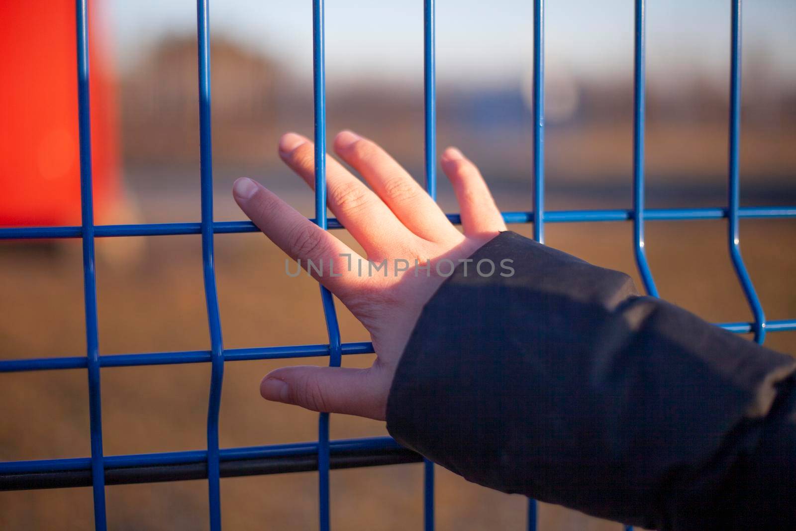 The girl holds her hand on the fence. Fingers cling to the bar. Metal obstacle. Forbidden territory. Private property. by OlegKopyov