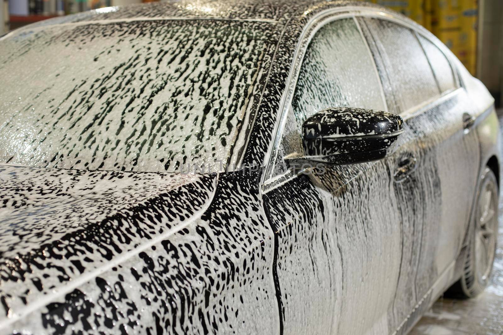 Car in car wash. Foam on car. White soapy solution. Cleaning of transport. Services in transport sector.